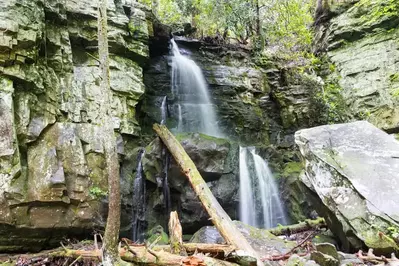 A beautiful waterfall flows over rocks on a scenic hiking trail.